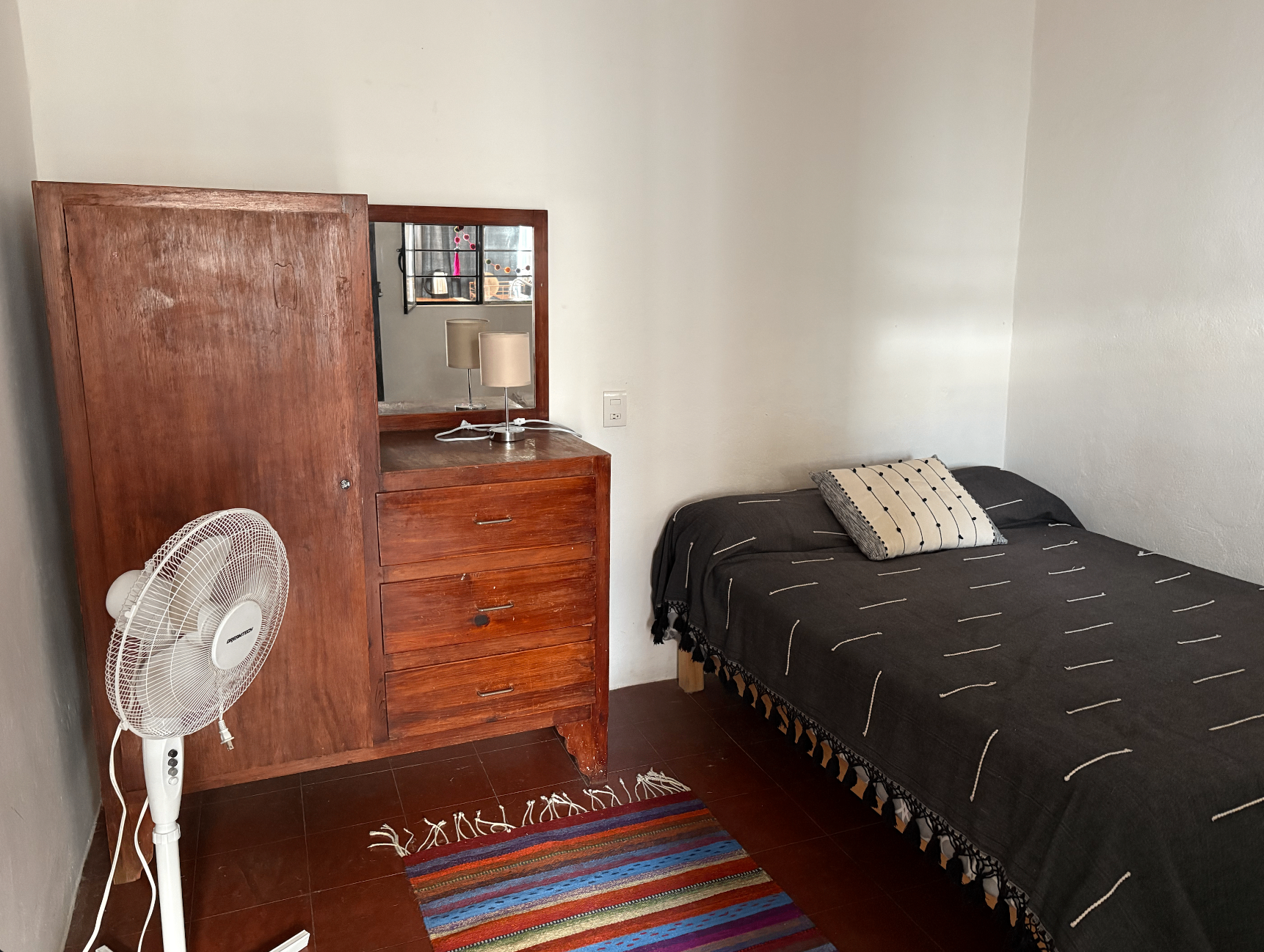 Private bedroom with wood wardrobe, dresser, and cozy bed with handwoven textiles.